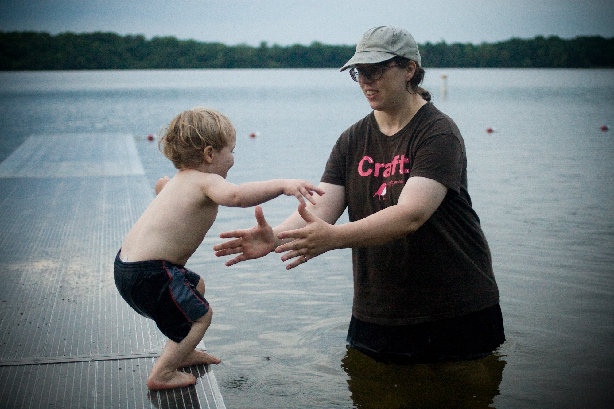 A small boy getting ready to jump off a dock into the arms of his mother