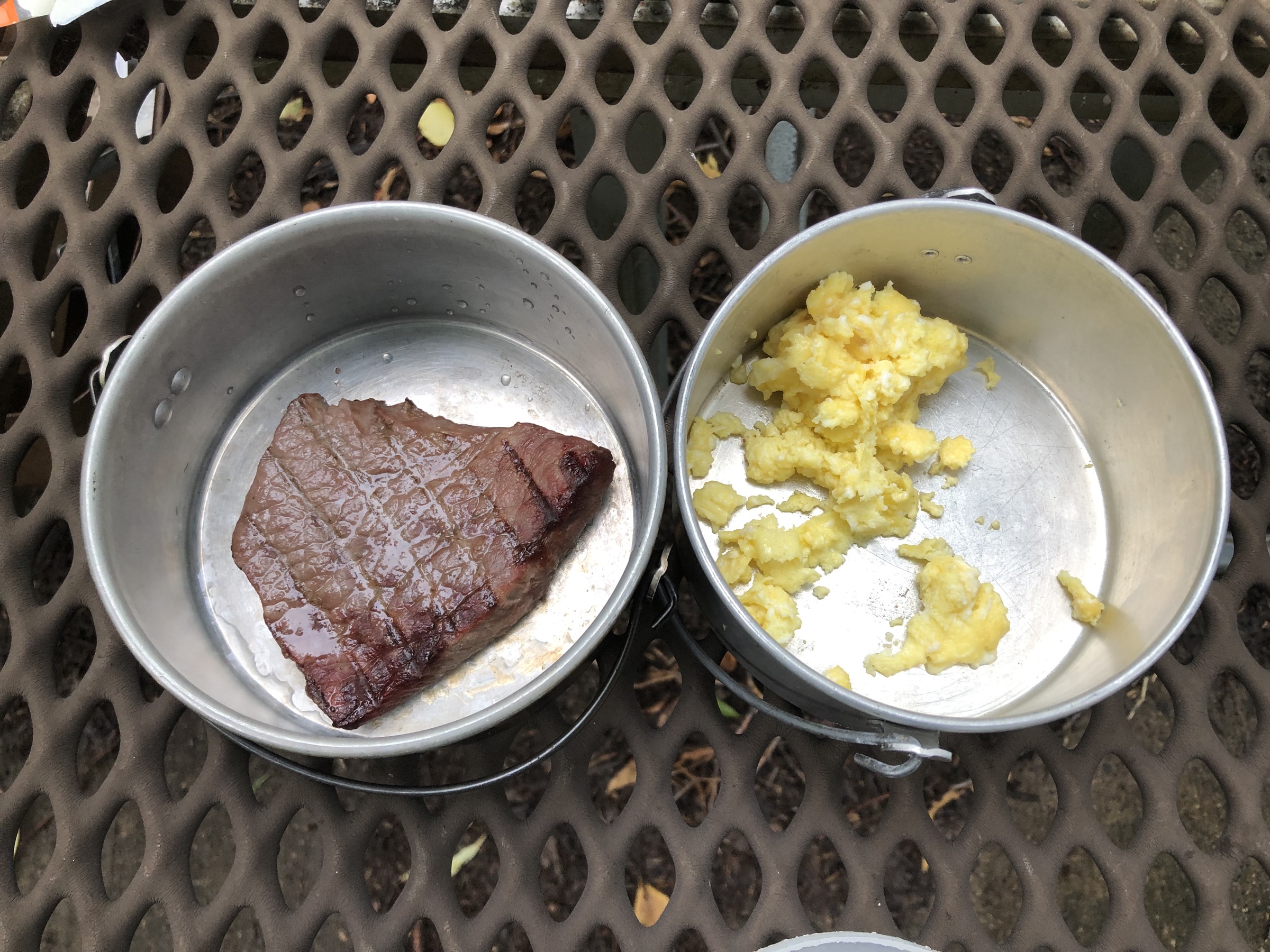 Two camping dishes, one with a small breakfast steak and one with partially eaten scrambled eggs