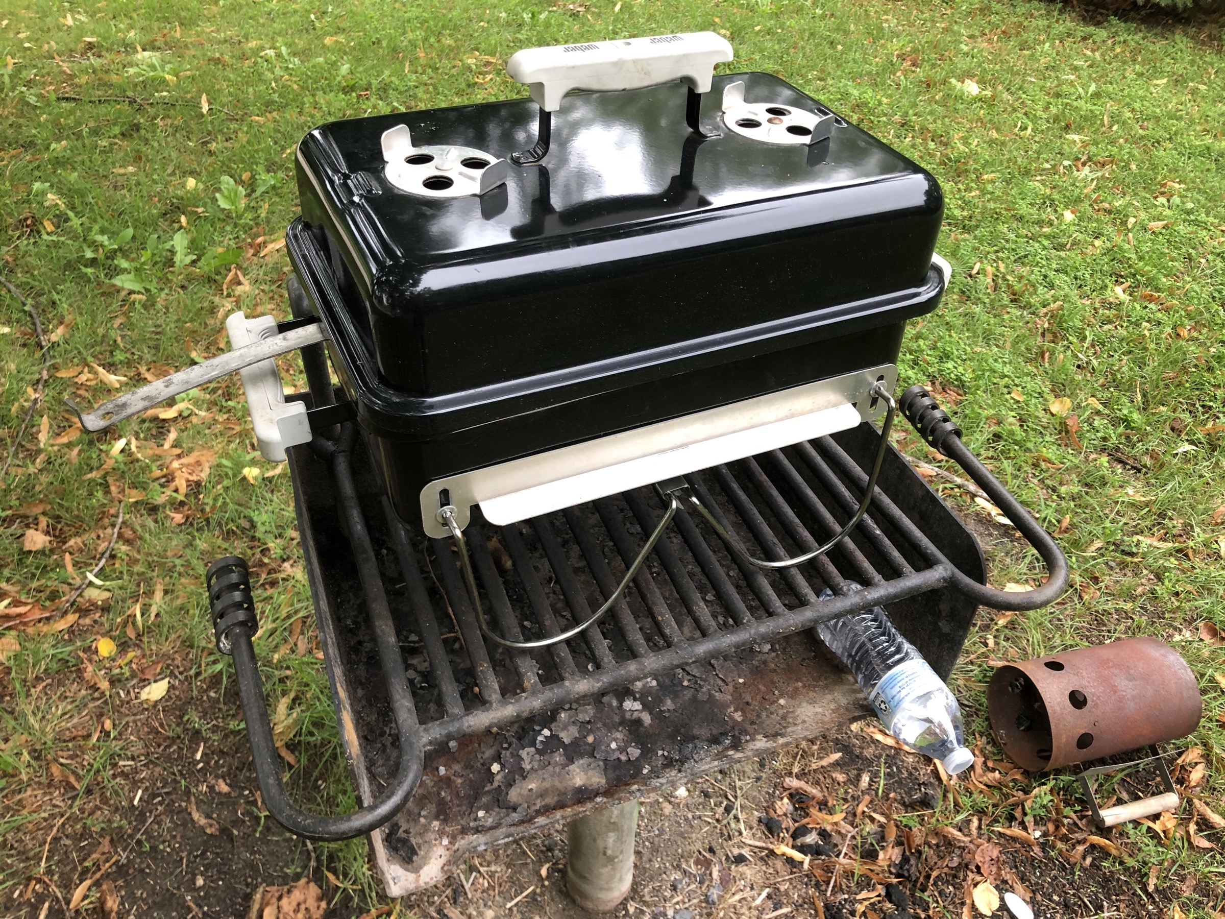 A Weber Go-Anywhere small rectangular charcoal grill sitting on top of a public grill