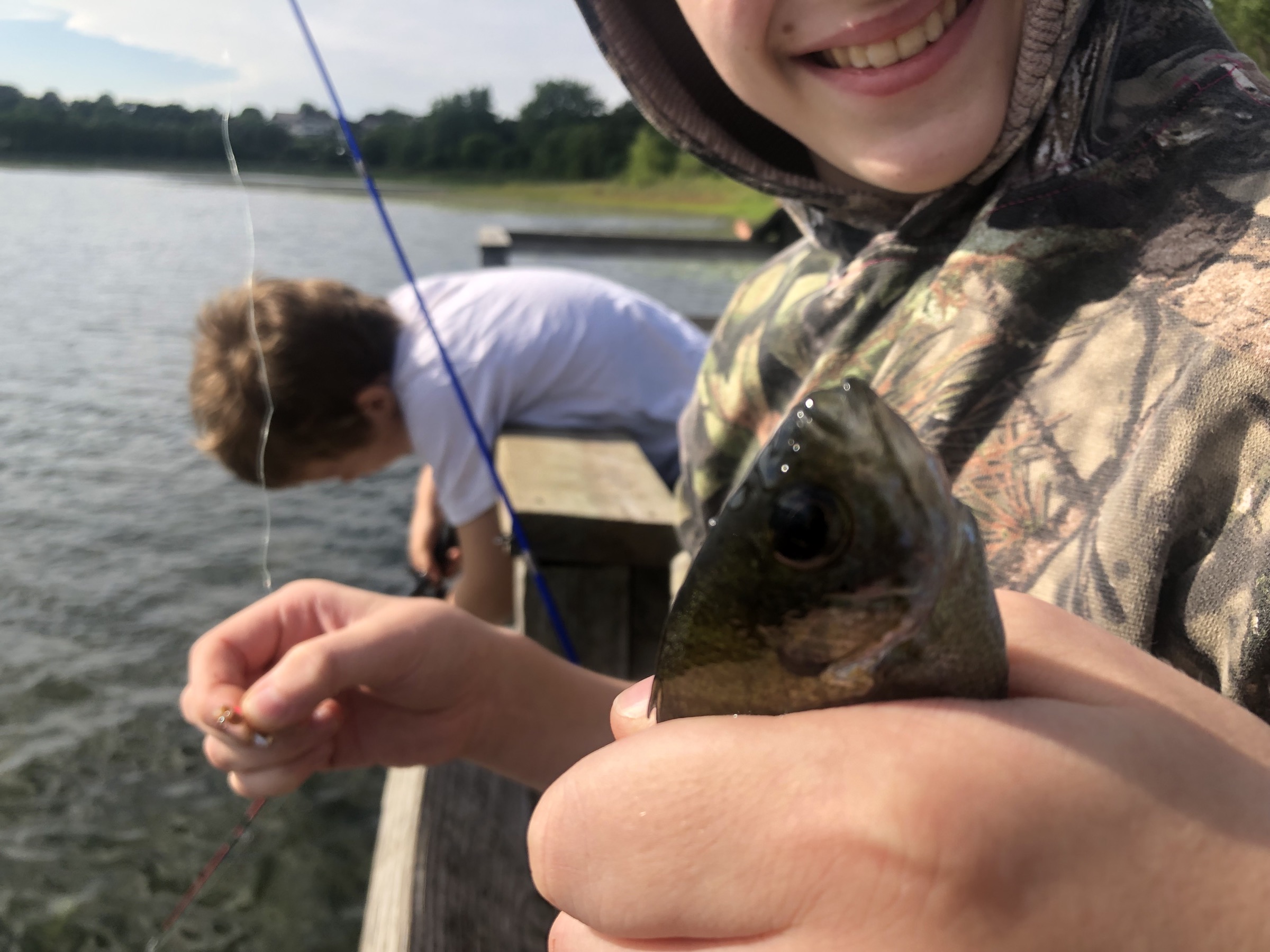 Two boys on a dock, one is holding up a small fish with one hand in the foreground