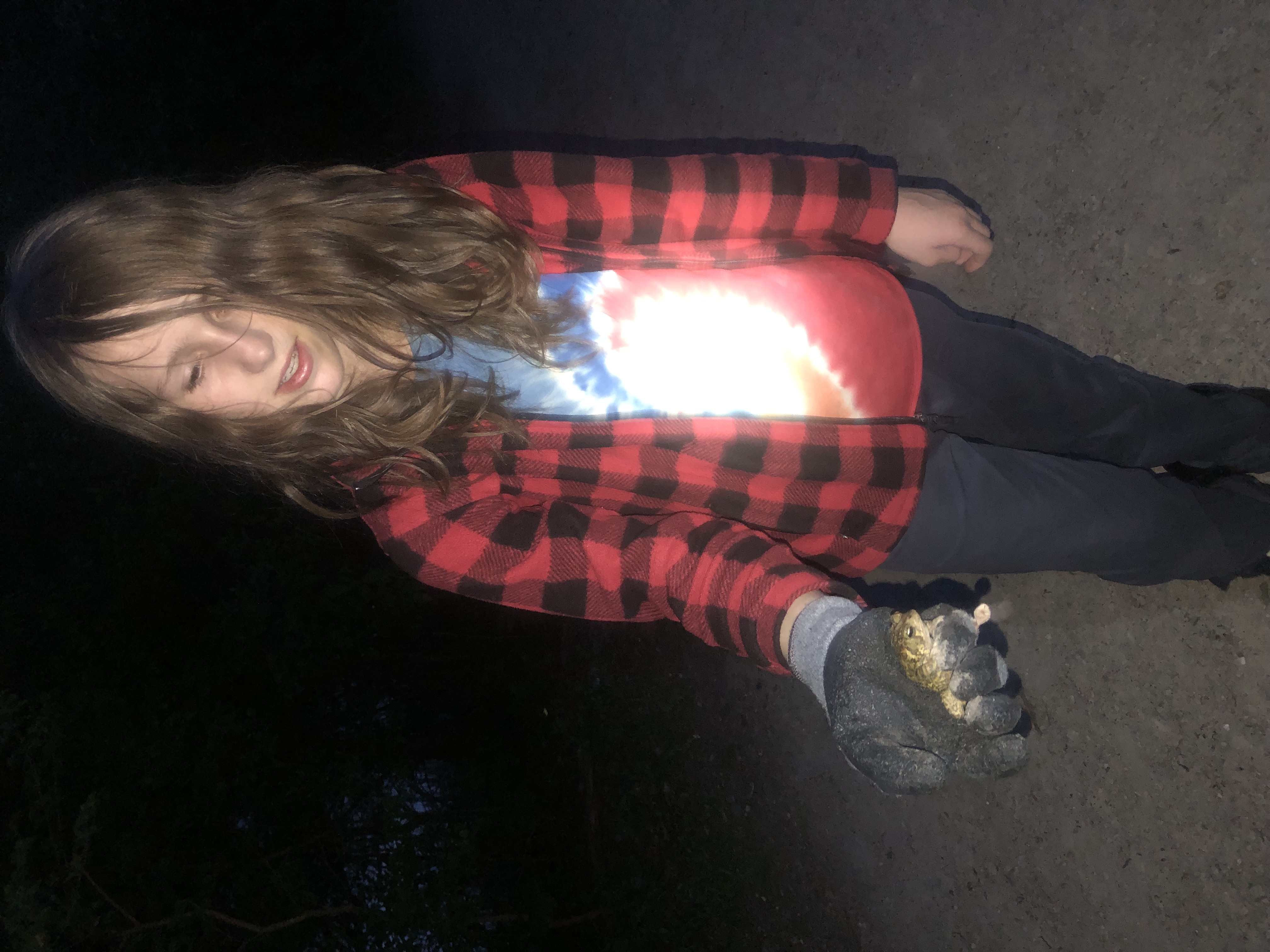 A boy with long hair in a red plaid shirt holding a frog